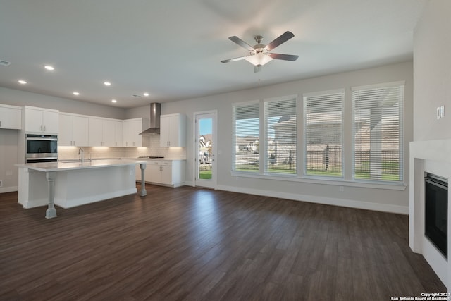 kitchen with dark wood-type flooring, white cabinets, plenty of natural light, and wall chimney range hood