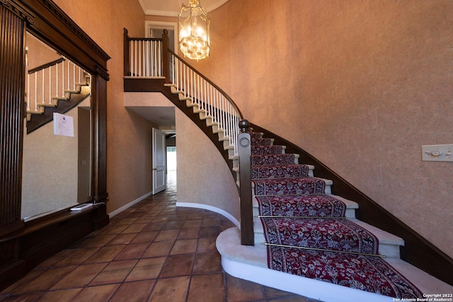 stairway with a towering ceiling, dark tile floors, and a chandelier