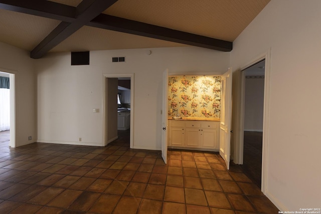 unfurnished bedroom featuring dark tile floors, ensuite bath, and beam ceiling