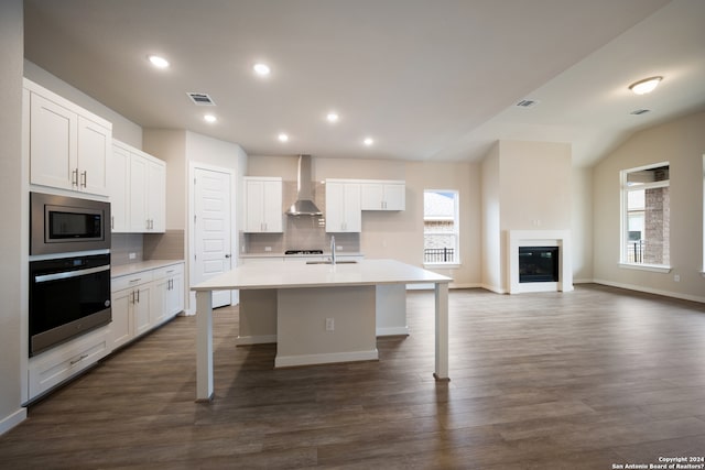 kitchen with white cabinets, wall chimney range hood, a kitchen island with sink, and appliances with stainless steel finishes