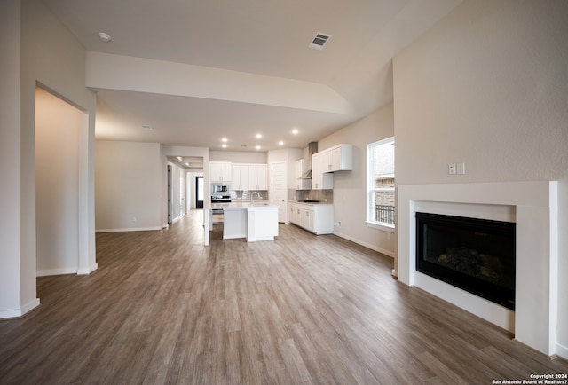 unfurnished living room featuring wood-type flooring, sink, and vaulted ceiling