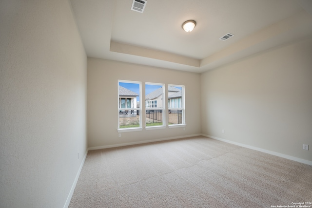 empty room with a raised ceiling and light carpet