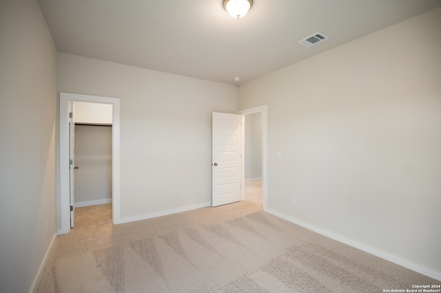 unfurnished bedroom featuring light colored carpet, a walk in closet, and a closet