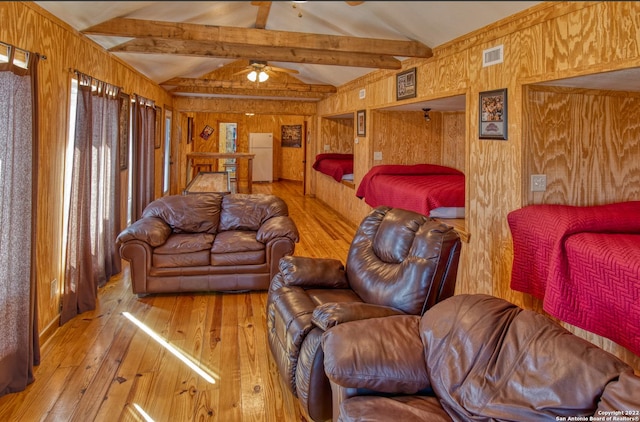 living room with light hardwood / wood-style flooring, lofted ceiling with beams, ceiling fan, and wooden walls