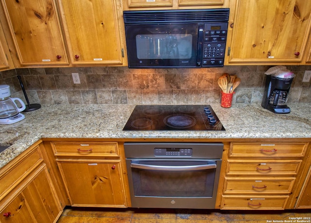 kitchen featuring light stone countertops, tasteful backsplash, and black appliances