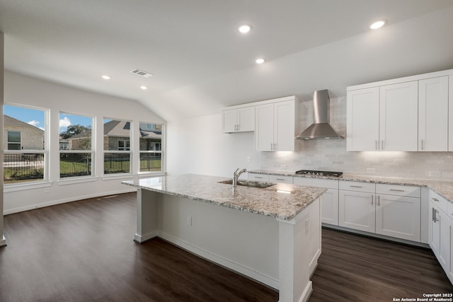 kitchen with wall chimney exhaust hood, dark hardwood / wood-style flooring, a kitchen island with sink, sink, and white cabinets