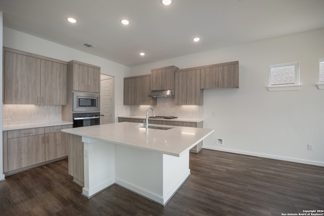 kitchen featuring dark wood-type flooring, appliances with stainless steel finishes, sink, an island with sink, and tasteful backsplash