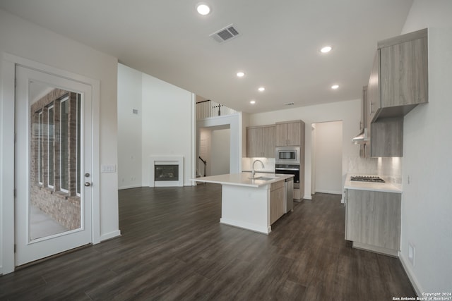 kitchen featuring appliances with stainless steel finishes, tasteful backsplash, sink, a kitchen island with sink, and dark hardwood / wood-style floors