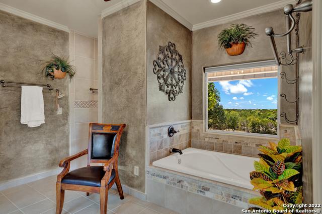 bathroom with tile flooring, crown molding, and tiled bath