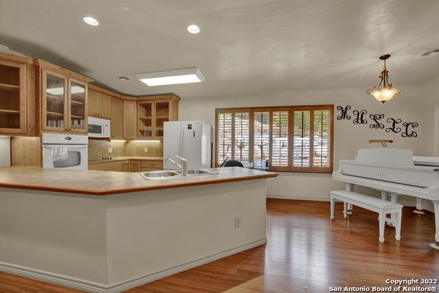 kitchen with hardwood / wood-style floors, hanging light fixtures, white appliances, sink, and tasteful backsplash