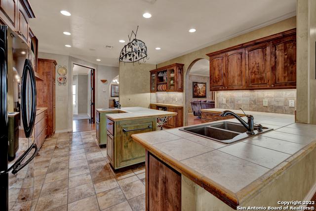 kitchen featuring backsplash, light tile flooring, sink, an island with sink, and black fridge