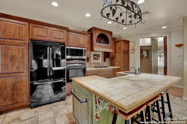 kitchen with premium range hood, light tile floors, black appliances, tile counters, and sink