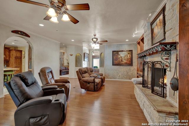 living room featuring ornamental molding, a fireplace, ceiling fan, and light wood-type flooring