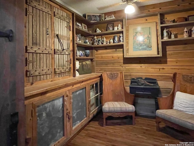 living area with wood walls, ceiling fan, and dark hardwood / wood-style flooring