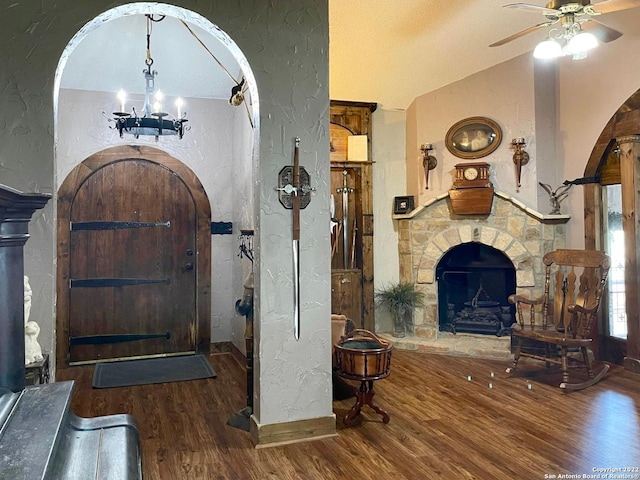 entrance foyer featuring vaulted ceiling, a textured ceiling, dark hardwood / wood-style flooring, ceiling fan with notable chandelier, and a stone fireplace