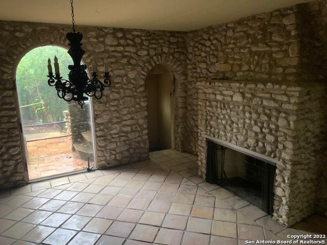 tiled empty room with a stone fireplace and an inviting chandelier