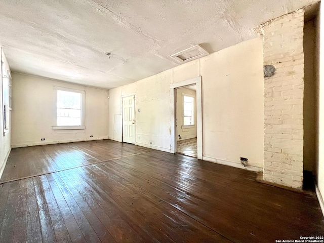 spare room featuring a textured ceiling, brick wall, and dark hardwood / wood-style flooring