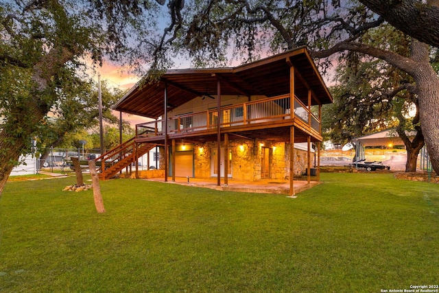 back house at dusk featuring a patio, a balcony, and a lawn