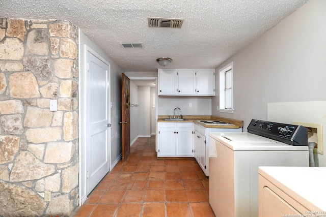 washroom featuring washing machine and dryer, a textured ceiling, sink, light tile flooring, and cabinets