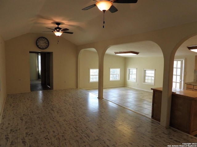 tiled empty room with plenty of natural light, vaulted ceiling, and ceiling fan