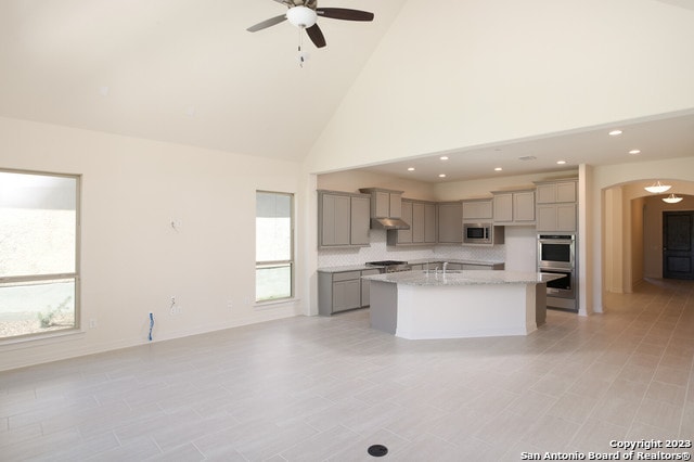 kitchen with an island with sink, ceiling fan, gray cabinets, stainless steel appliances, and high vaulted ceiling