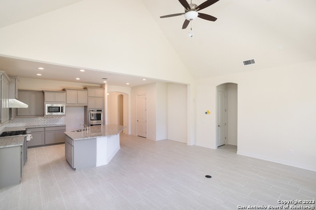 kitchen with appliances with stainless steel finishes, ceiling fan, high vaulted ceiling, a kitchen island with sink, and gray cabinets