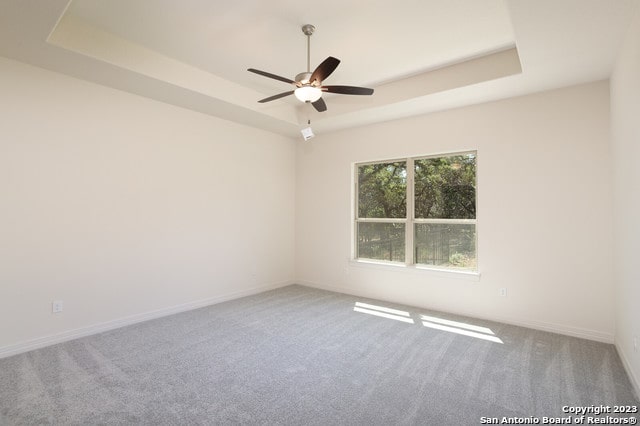 carpeted empty room with ceiling fan and a raised ceiling