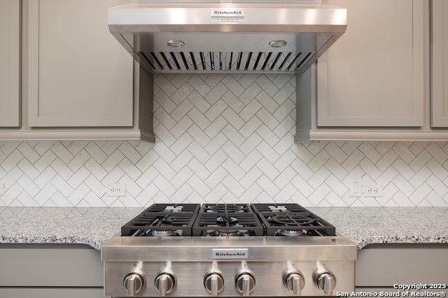 kitchen with light stone countertops, backsplash, and wall chimney exhaust hood