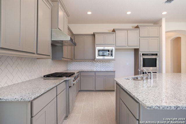 kitchen featuring light stone countertops, backsplash, appliances with stainless steel finishes, sink, and wall chimney exhaust hood