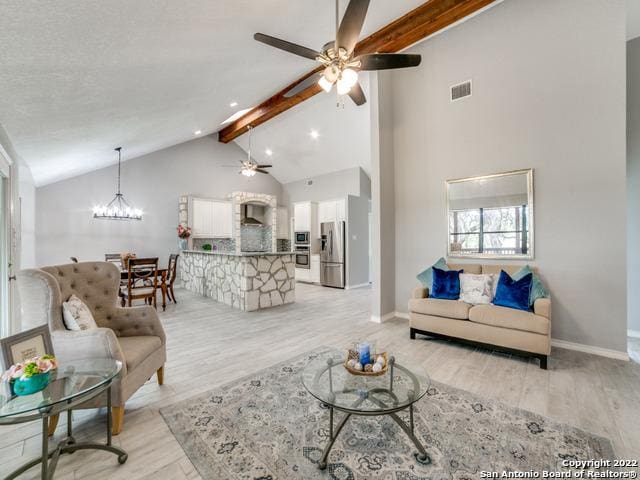 living room with high vaulted ceiling, ceiling fan with notable chandelier, light wood-type flooring, and beamed ceiling