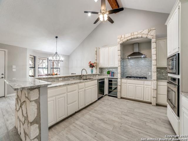 kitchen featuring kitchen peninsula, beverage cooler, wall chimney range hood, ceiling fan with notable chandelier, and vaulted ceiling with beams