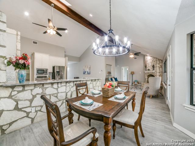 dining area with a stone fireplace, light wood-type flooring, high vaulted ceiling, ceiling fan with notable chandelier, and beam ceiling