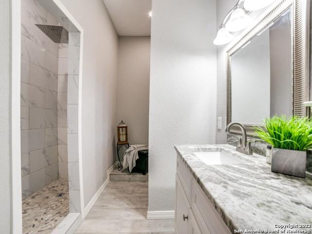 bathroom with oversized vanity, a tile shower, and wood-type flooring