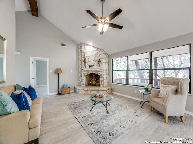 living room featuring high vaulted ceiling, beam ceiling, ceiling fan, a stone fireplace, and light hardwood / wood-style flooring