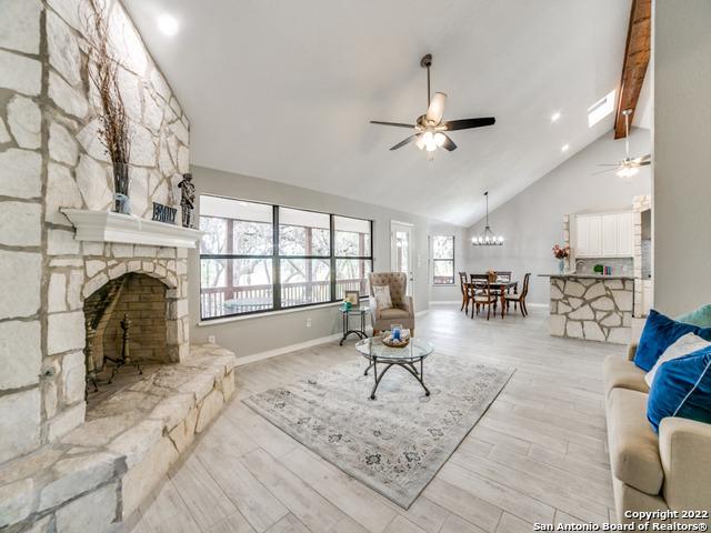 living room featuring high vaulted ceiling, beam ceiling, ceiling fan with notable chandelier, a stone fireplace, and light wood-type flooring