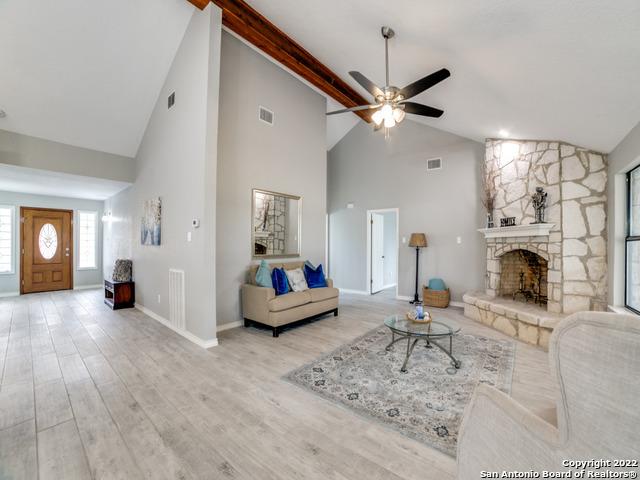 living room featuring high vaulted ceiling, a fireplace, light wood-type flooring, ceiling fan, and beam ceiling