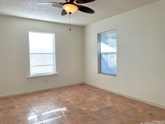 tiled empty room featuring ceiling fan, a textured ceiling, and a healthy amount of sunlight