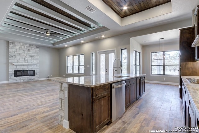 kitchen with light stone countertops, stainless steel appliances, a kitchen island with sink, sink, and a stone fireplace