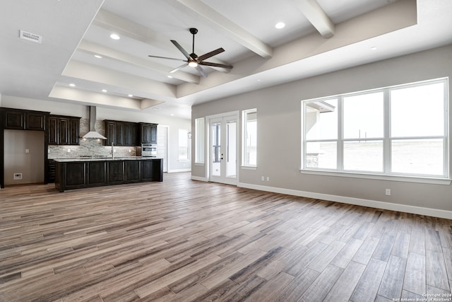 unfurnished living room with french doors, a raised ceiling, ceiling fan, beam ceiling, and light hardwood / wood-style flooring