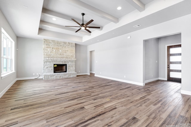 unfurnished living room featuring beam ceiling, ceiling fan, a fireplace, and light hardwood / wood-style flooring