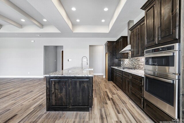 kitchen with appliances with stainless steel finishes, light hardwood / wood-style floors, light stone counters, and a kitchen island with sink