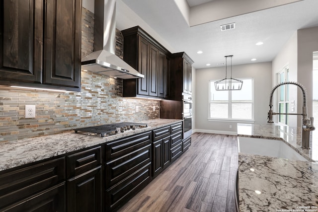 kitchen featuring sink, wall chimney range hood, decorative light fixtures, appliances with stainless steel finishes, and hardwood / wood-style flooring