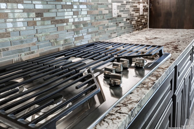 interior details featuring stove, backsplash, light stone counters, and stainless steel gas stovetop