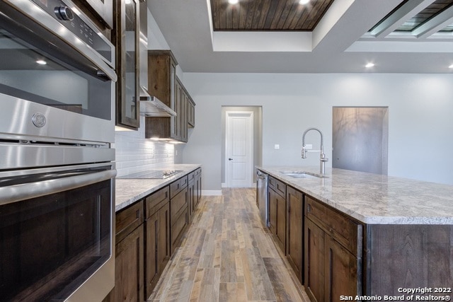 kitchen featuring sink, stainless steel appliances, tasteful backsplash, an island with sink, and hardwood / wood-style flooring