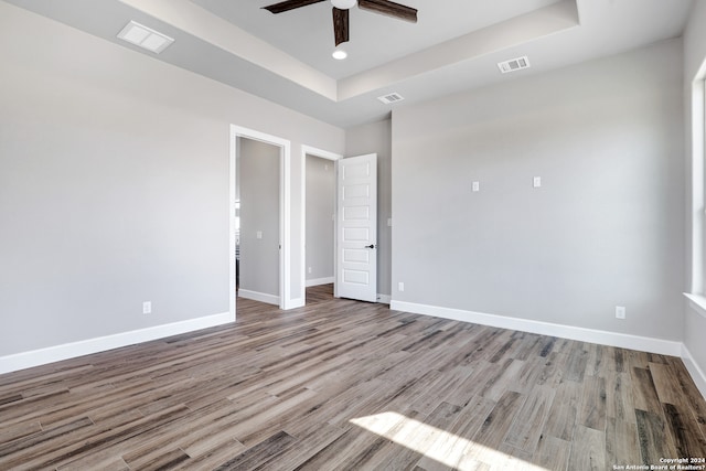 unfurnished bedroom featuring ceiling fan, light wood-type flooring, and a tray ceiling