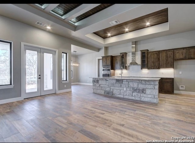 kitchen featuring french doors, tasteful backsplash, a tray ceiling, wall chimney range hood, and a center island