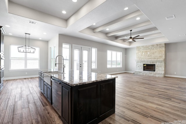 kitchen featuring light stone countertops, wood-type flooring, a tray ceiling, a kitchen island with sink, and a fireplace