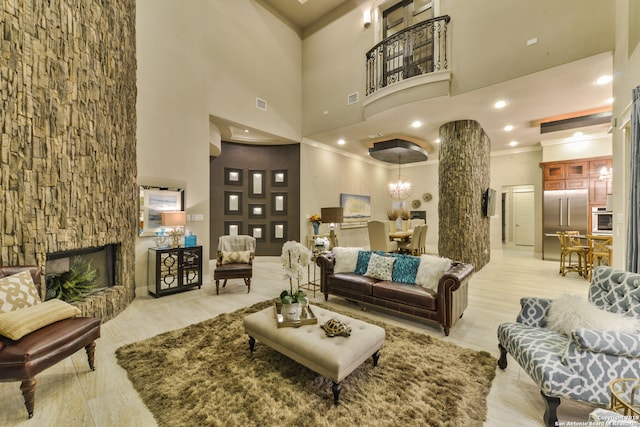 living room featuring an inviting chandelier, a stone fireplace, crown molding, light wood-type flooring, and a high ceiling