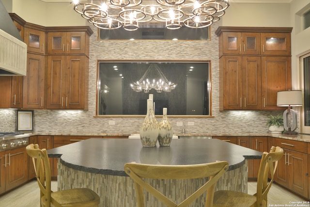 interior space featuring pendant lighting, tasteful backsplash, light stone counters, a breakfast bar area, and an inviting chandelier