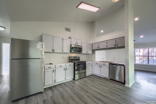 kitchen with white cabinets, appliances with stainless steel finishes, high vaulted ceiling, and hardwood / wood-style floors